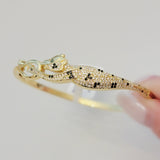 Close-up of the Wild Mosaic Cheetah Bangle showing detailed black and white CZ mosaic spots, green CZ eyes, and gold-plated cheetah design holding its tail.