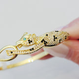 Close-up of the Wild Mosaic Cheetah Bangle showing detailed black and white CZ mosaic spots, green CZ eyes, and gold-plated cheetah design holding its tail.