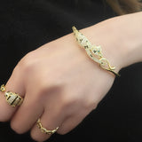 Close-up of the Wild Mosaic Cheetah Bangle showing detailed black and white CZ mosaic spots, green CZ eyes, and gold-plated cheetah design holding its tail.