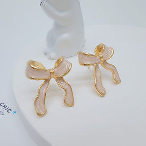 Close-up of the Bubblegum Bow Studs featuring delicate titanium steel bows coated in glossy pink enamel with gold-plated accents. The enamel's smooth finish and the detailed bow shape reflect light softly, highlighting the sweet, whimsical design.


