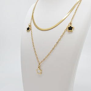 Close-up of the Twilight Stars Necklace showing fine details of the black and white enamel star charms on an 18K gold plated titanium steel chain. The stars have a smooth, glossy finish that contrasts beautifully against the gold.