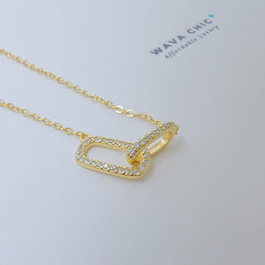 Close-up image of the Clip Lock Necklace showing the detailed craftsmanship of the clip pendant, sparkling cubic zirconia accents, and the smooth 14K gold-plated sterling silver chain. The textures and refined shine highlight the modern industrial design.