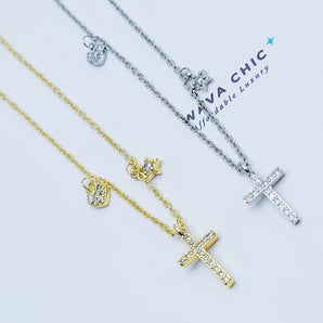 Close-up of the Mini Grace Necklace showcasing the polished sterling silver cross pendant, with a delicate CZ heart charm and a tiny star charm dangling asymmetrically on either side. The craftsmanship highlights shine, detail, and delicate proportions.
