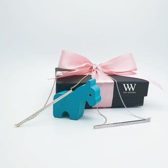 A photo of diamond bar necklaces on signature Jewelry box, wrapped with ribbons and decorative a toy horse. 